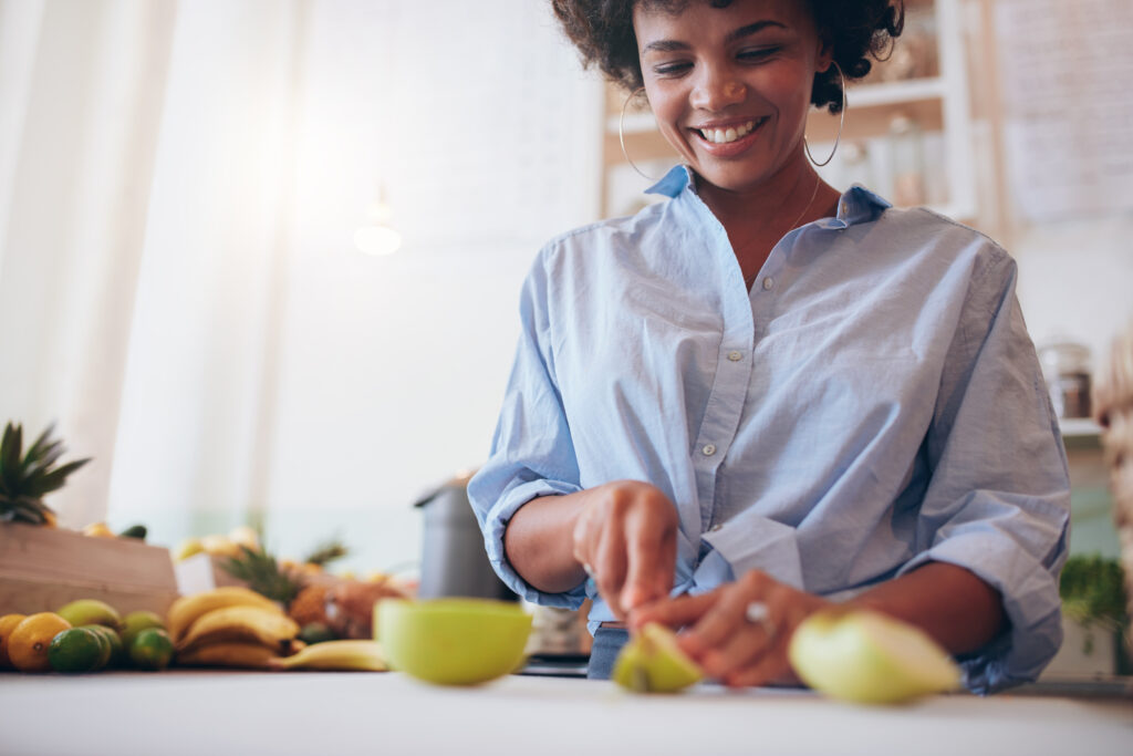 woman smiling cutting an apple with other fresh produce around her.
photo by adobe stock