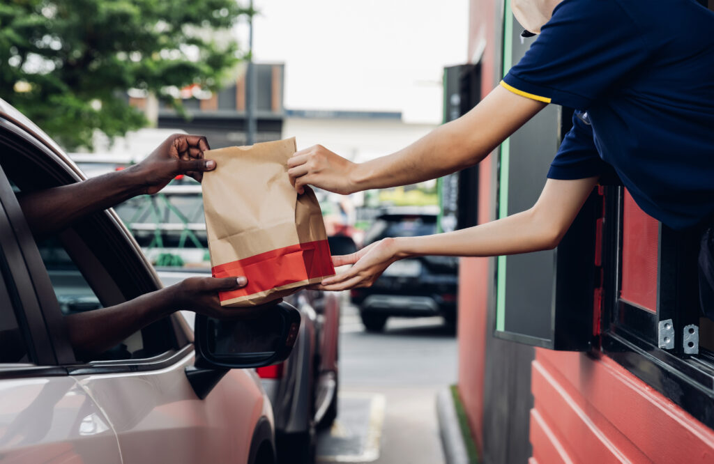 Fast food worker handing bag of food from building window to customer in vehicle in the drive through.
Picture by Kanpisut.