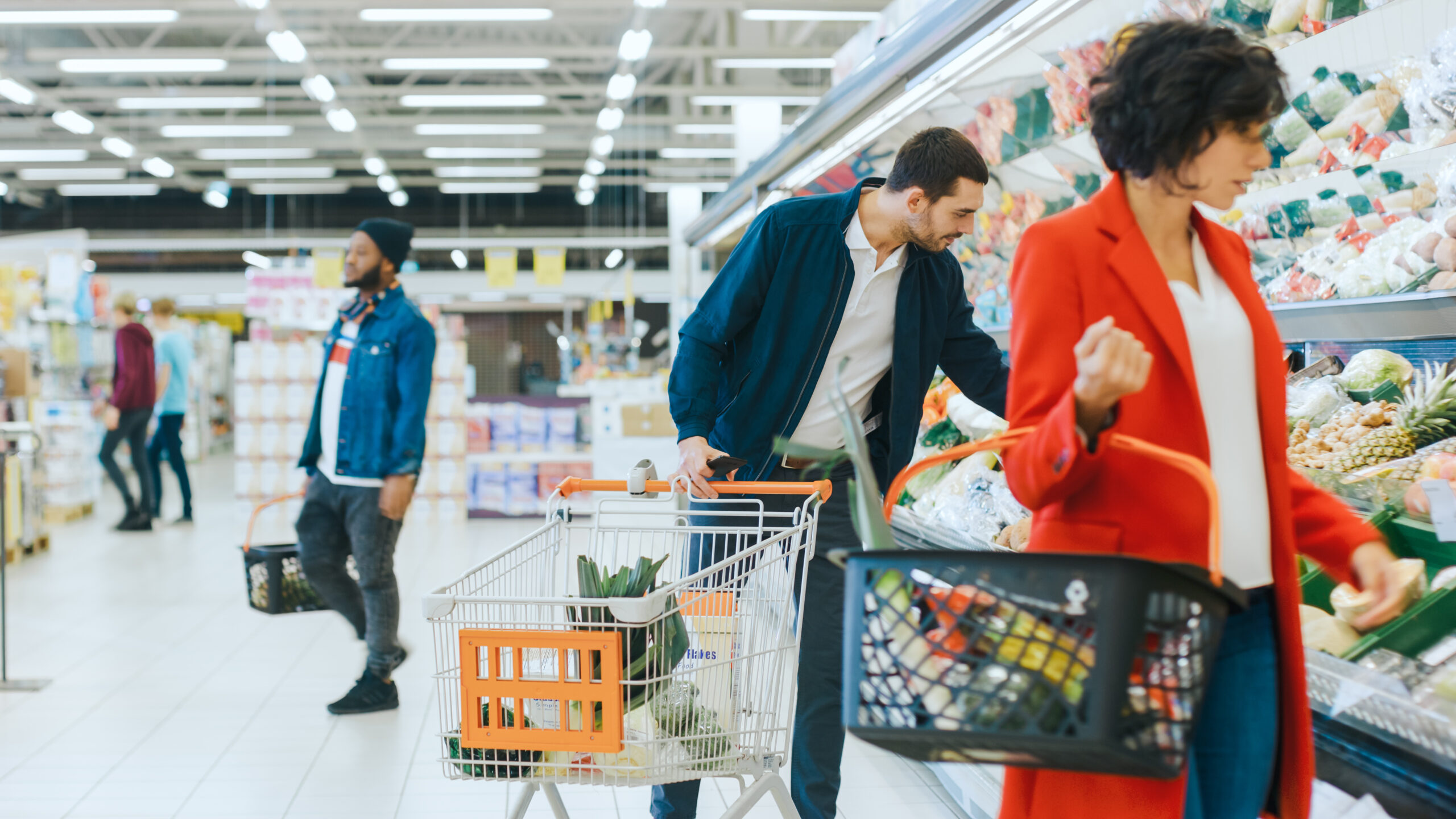 At the Supermarket: Handsome Man with Smartphone, Pushes Shopping Cart, Walks Through Fresh Produce Section of the Store, Chooses Some Products. Other Customers Purchasing Products.
By Gorodenkoff